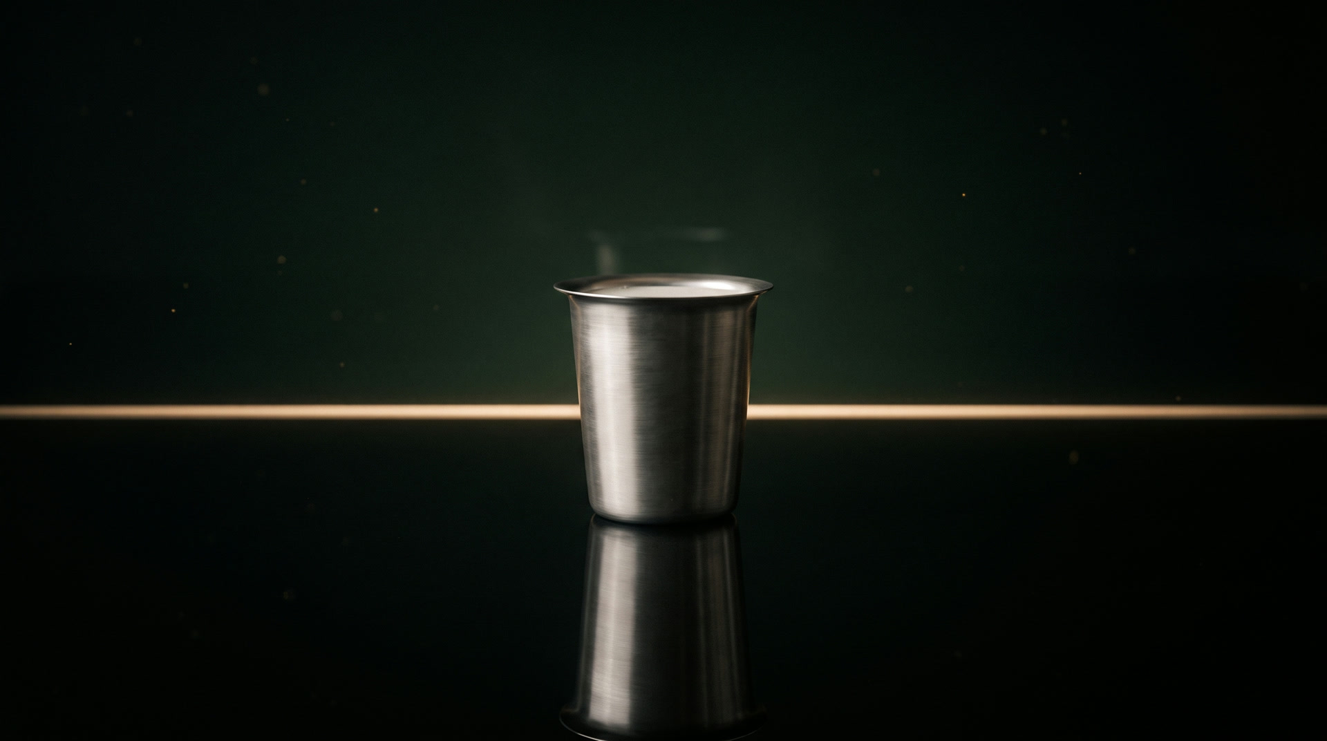 A plain steel chai tumbler standing on still dark water, lit by one thin line of light.