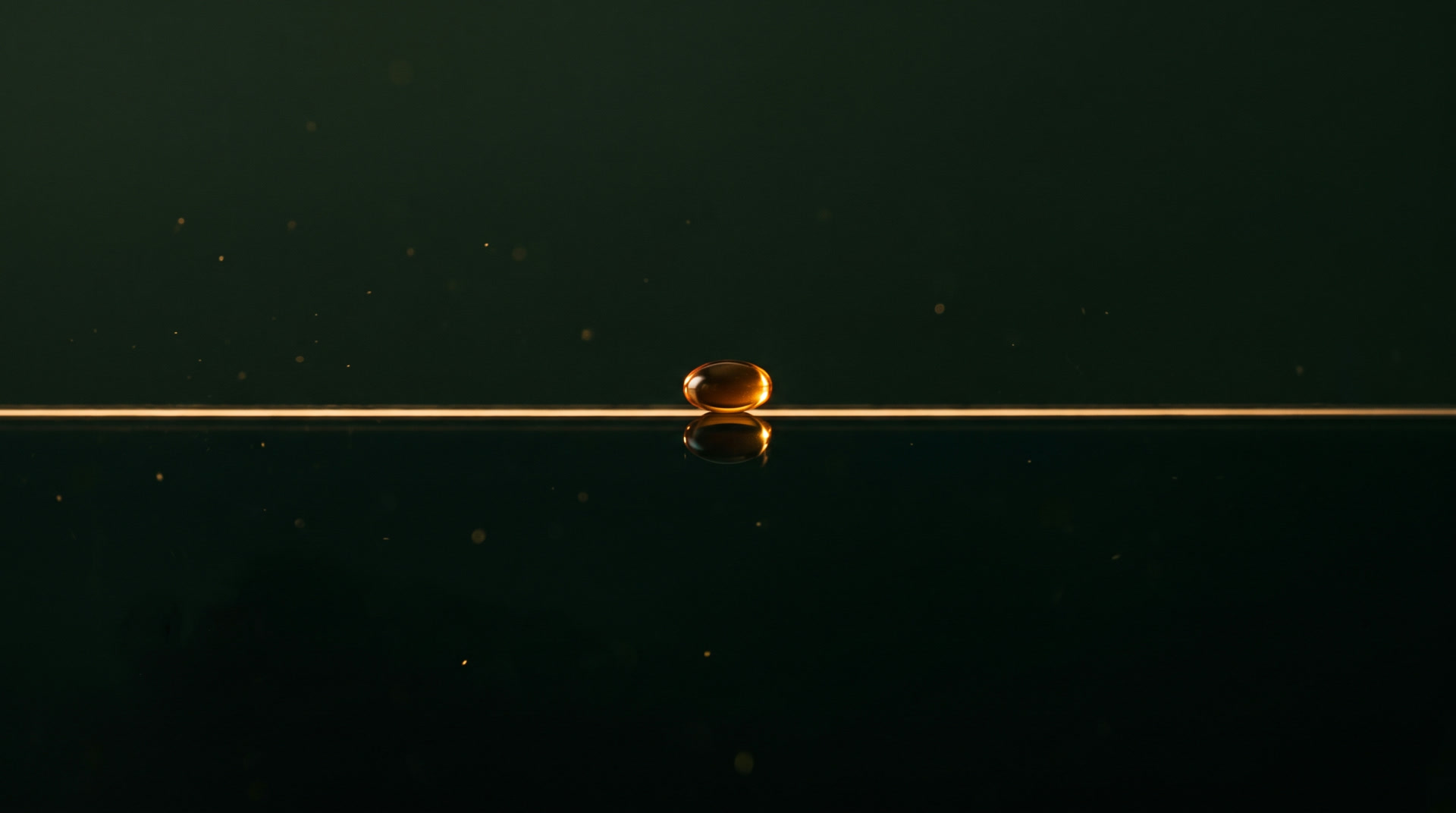 A single small amber softgel resting on the line of light above still dark water.