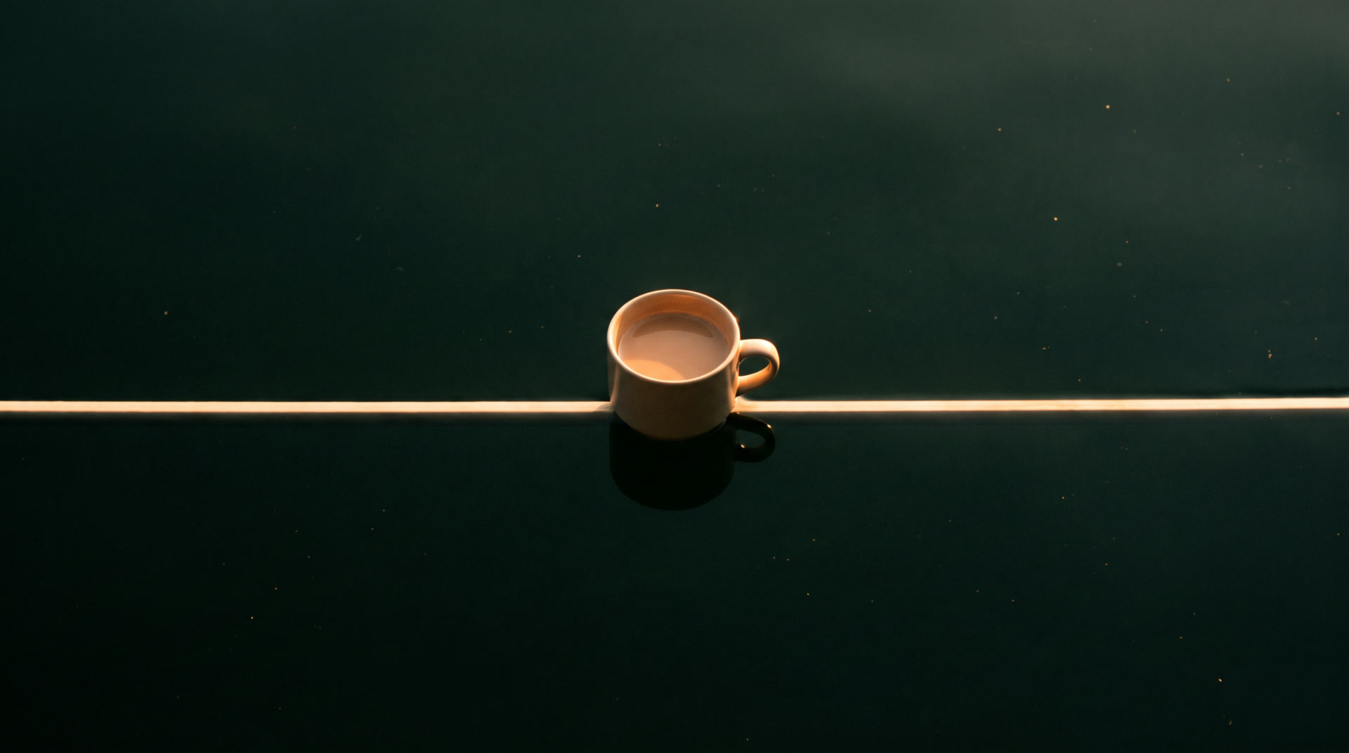 A plain ceramic cup of chai resting on the line of light above still dark water.